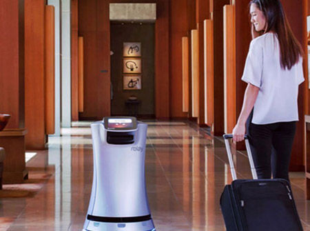 Woman with rolling suitcase in hotel lobby walking with service robot